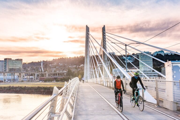 Two people riding bikes over a bridge in Portland, Oregon during sunset